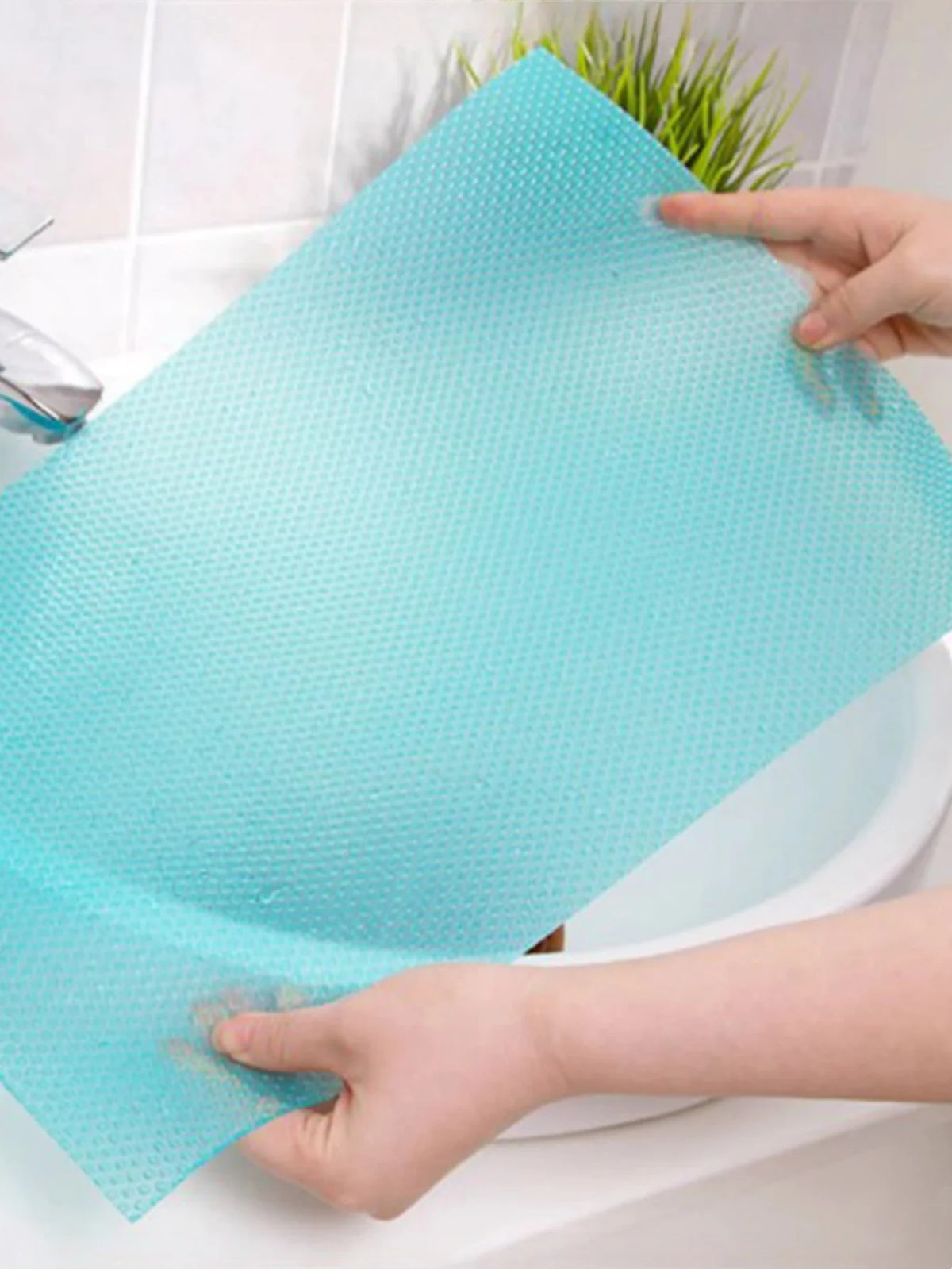 A hand is placing a light blue, textured shelf liner into a white porcelain sink or tub.