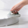 A hand is holding a light green magic sponge scrubber with a long handle, resting on a white toilet bowl.