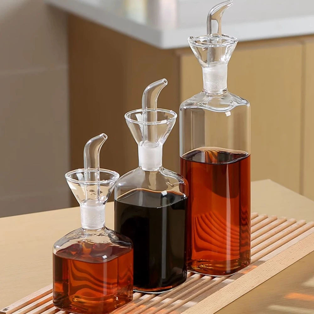 A set of clear borosilicate glass oil and vinegar dispensers with white stoppers sitting on a wooden surface.