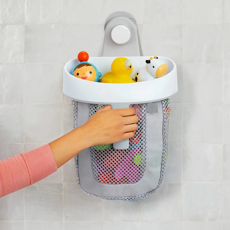 A hand is placing a white hanging bath toy storage bag with a light gray mesh onto a tile wall.