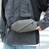 A person wearing a gray waterproof jacket is holding a gray minimalist running waist pack.