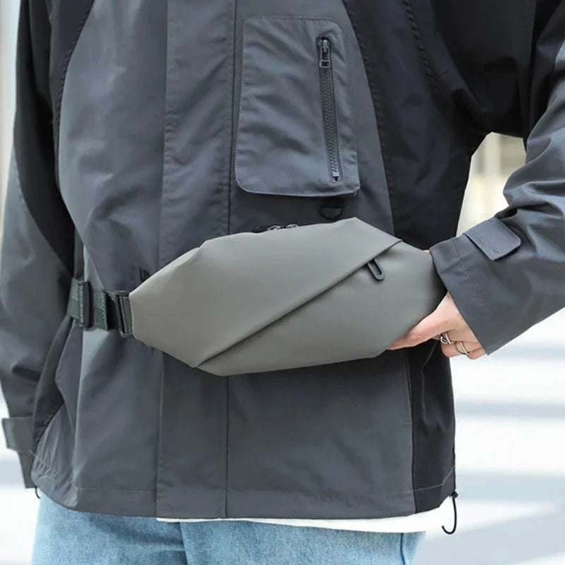 A person wearing a gray waterproof jacket is holding a gray minimalist running waist pack.