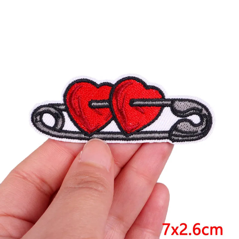 A hand holds a red heart embroidery patch shaped like a cartoon cat, ready for iron-on application.