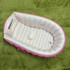 Pink inflatable bathtub for babies and toddlers with a hand pump resting on green fabric.
