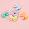 A collection of five pastel silicone bow beads in light blue, gray, purple, yellow, and orange arranged on a pink background.