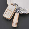 A white TPU protective key case with gold accents and a silver keyring attached to a leather strap.