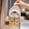 A hand is holding a fluffy, light brown penguin plush toy with a white hat and yellow feet.