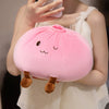 Un coussin en forme de dumpling rose rond avec de petites oreilles brunes est tenu par une personne.