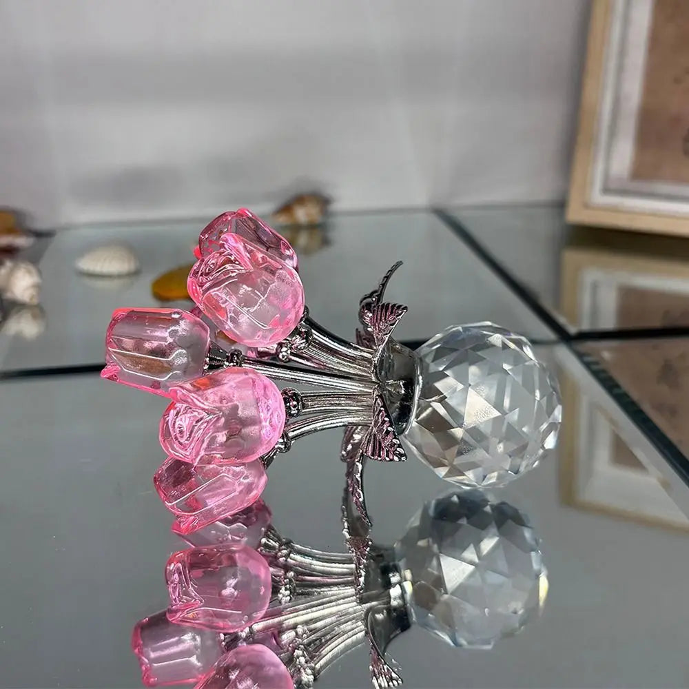 A crystal rose sculpture with a bouquet of pink and clear reflective crystals displayed on a glass surface.