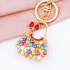 A gold-toned handbag keychain featuring colorful crystal and rhinestone embellishments on a pink fabric background.