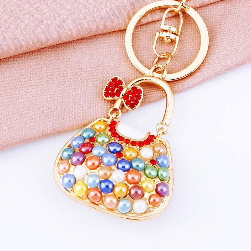 A gold-toned handbag keychain featuring colorful crystal and rhinestone embellishments on a pink fabric background.