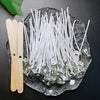 A collection of white cotton candle wicks with metal stands is displayed on a dark surface next to a wooden stand.