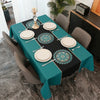 A rectangular table set for dining with a teal tablecloth, black and teal placemats featuring geometric patterns, and gray ch