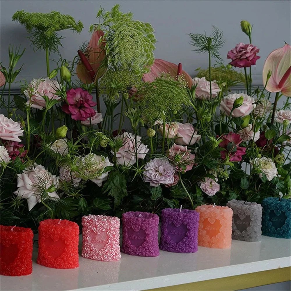A collection of pink and green roses and foliage arranged on a white surface with various colored pillar candles.
