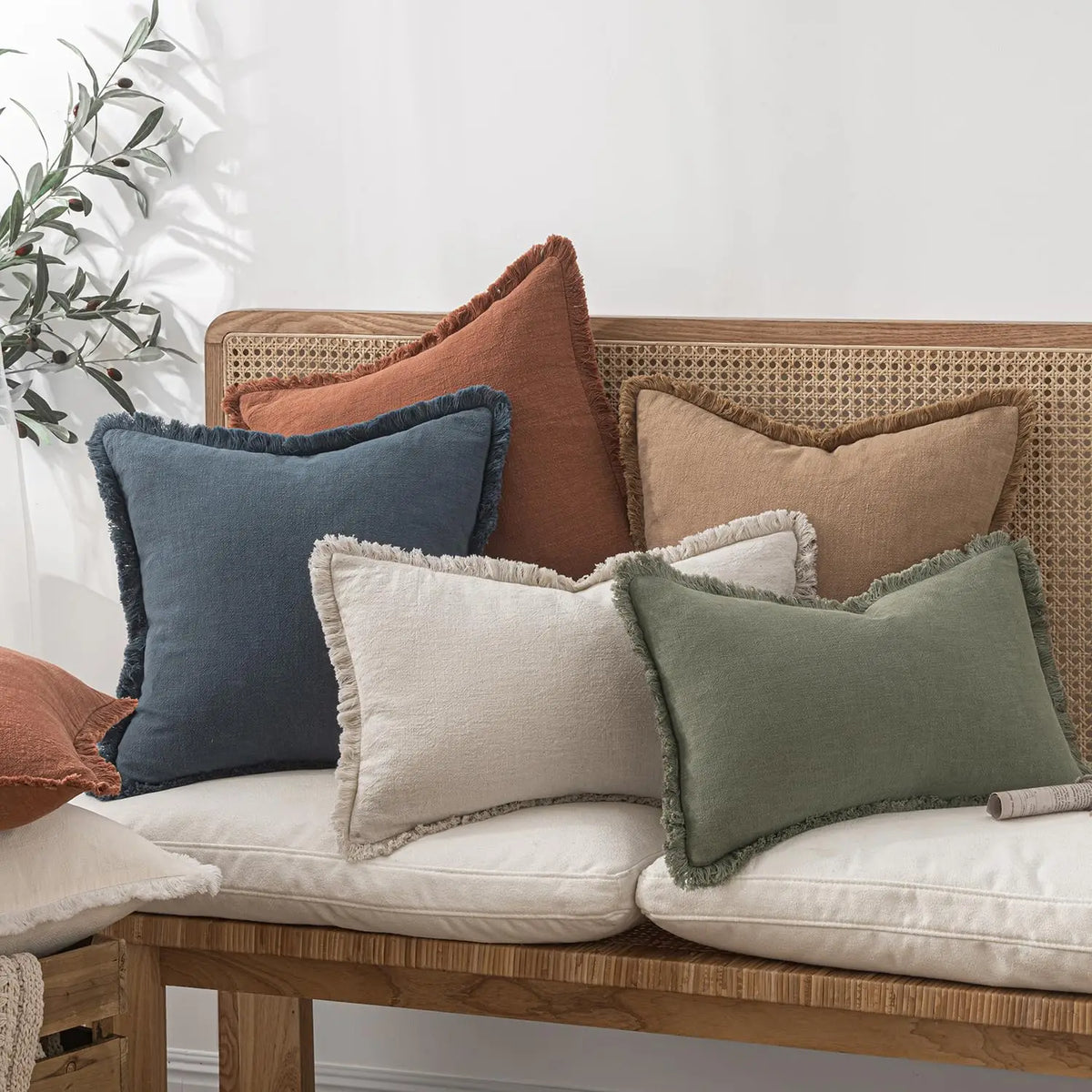 A collection of linen-textured throw pillows in earthy tones including terracotta, olive green, beige, and dusty blue on a wo