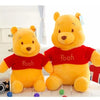 A yellow Winnie the Pooh plush toy bear wearing a red shirt sitting next to a camera.