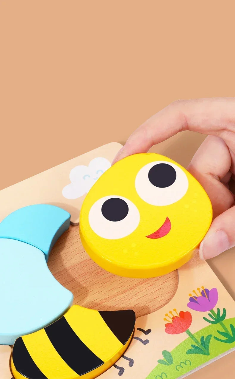A hand is holding a yellow puzzle piece shaped like a smiling bee, part of a wooden learning toy set.
