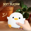 A hand is gently pinching a white silicone duck night light, which is illuminated and has a touch control feature.
