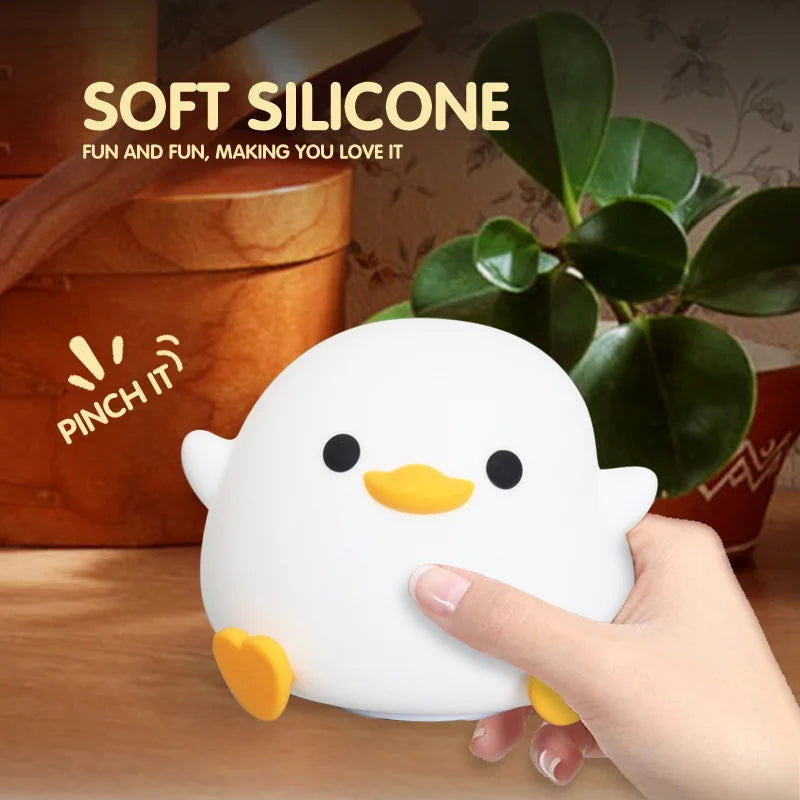A hand is gently pinching a white silicone duck night light, which is illuminated and has a touch control feature.