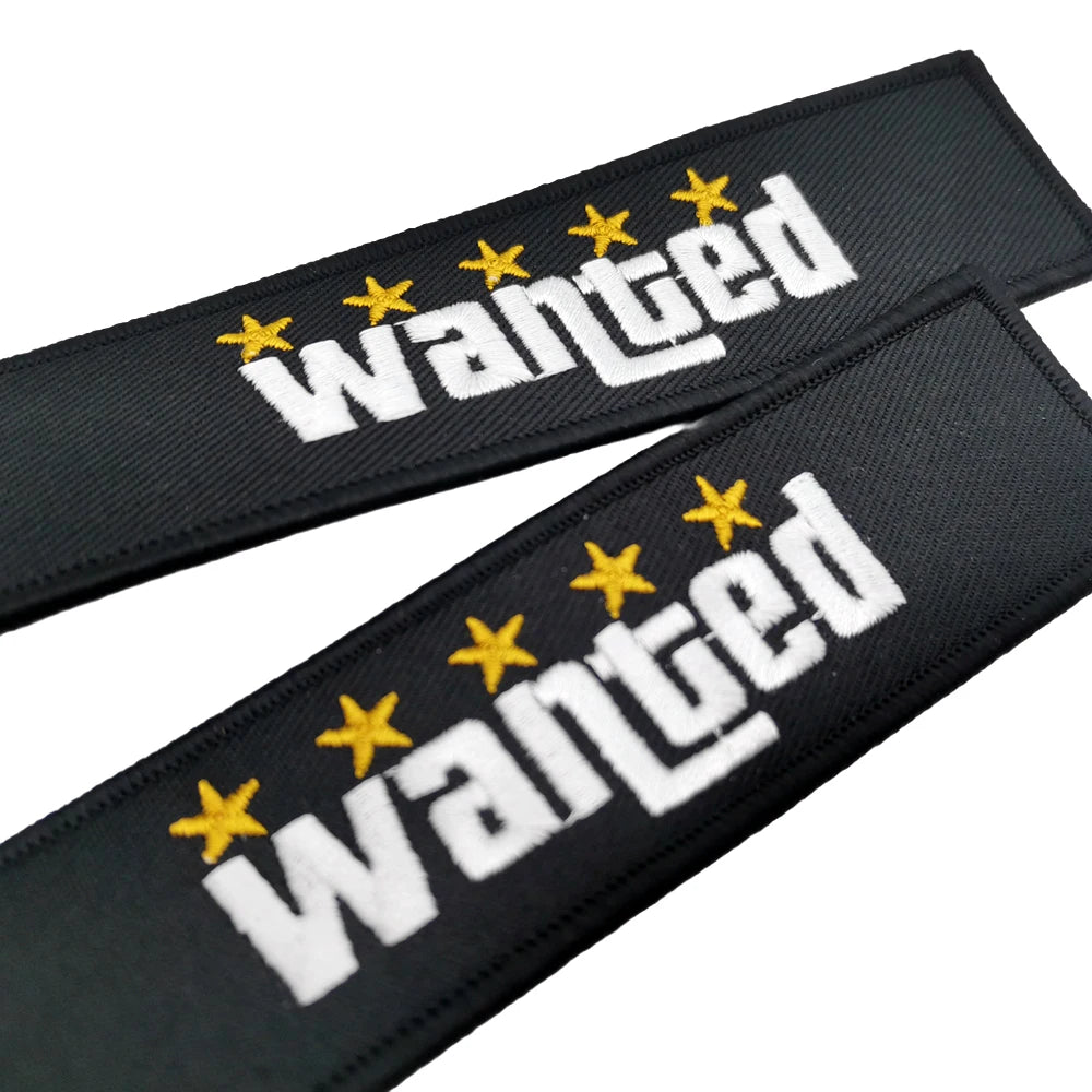 Black nylon keychain with white embroidered text WANTED and yellow stars on a black background