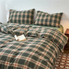 A plaid duvet cover in olive green and burgundy tones with a tartan pattern displayed on a bed.