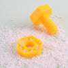 A yellow plastic screw and nut building block resting on a white granular surface.