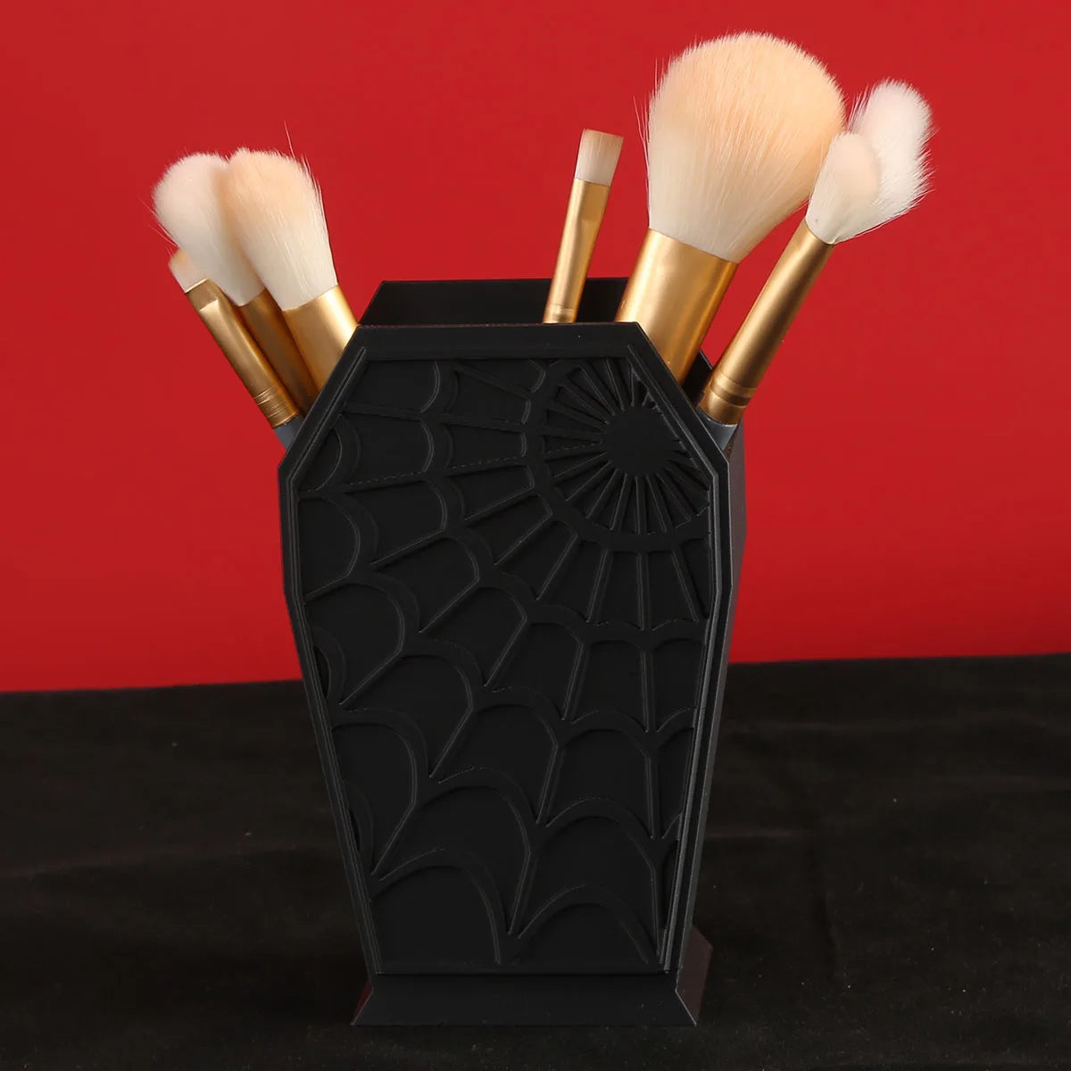 Black coffin-shaped makeup brush holder with a spider web design and several fluffy makeup brushes.
