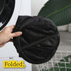 A hand holds a black foldable laundry hamper with a textured mesh fabric.