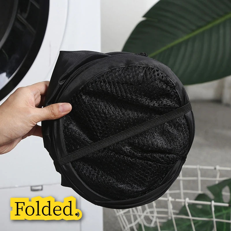 A hand holds a black foldable laundry hamper with a textured mesh fabric.