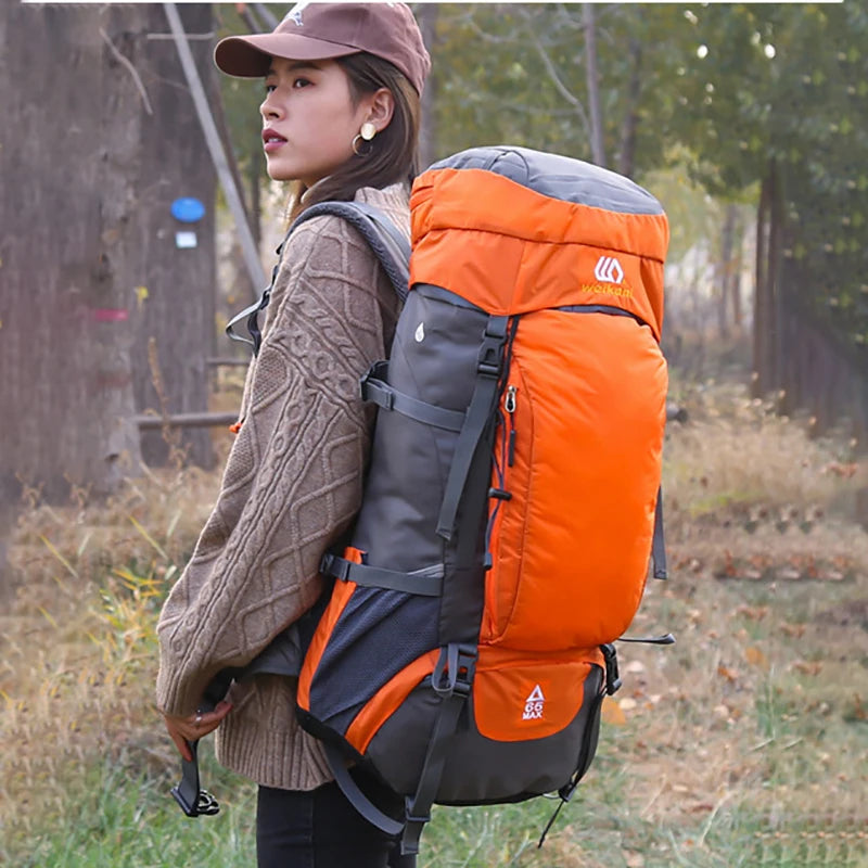 A woman is holding an orange and gray waterproof hiking backpack outdoors in a natural setting.