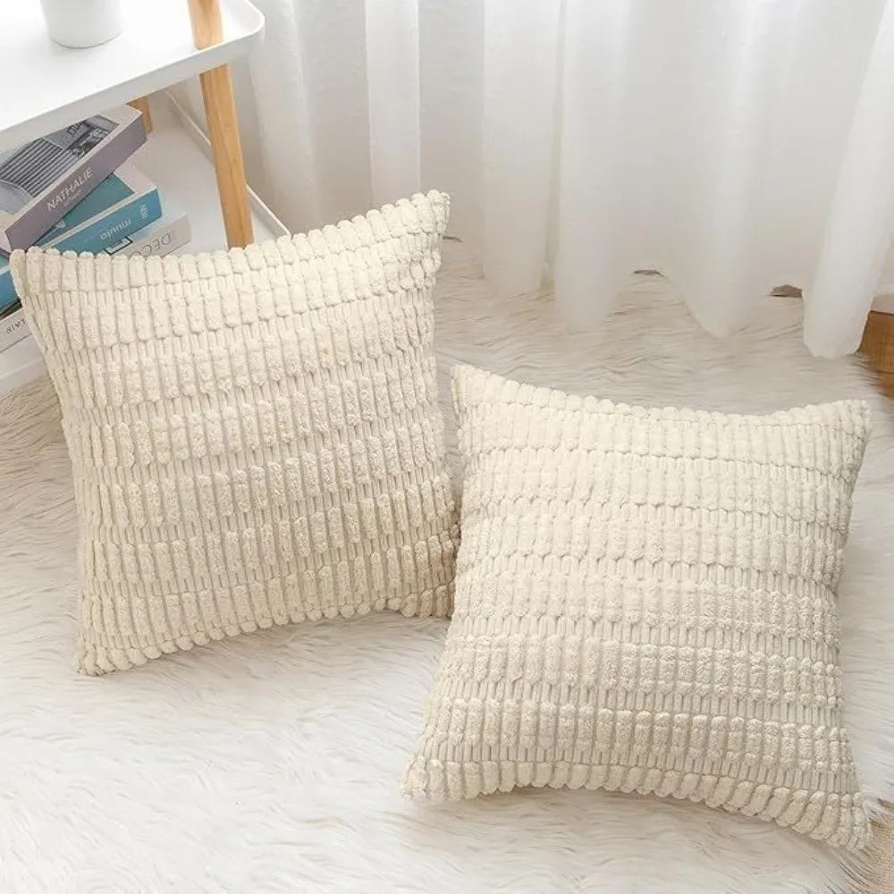 A pair of cream-colored knitted pillows with a ribbed texture displayed on a white surface.