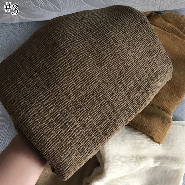A dark brown, ribbed fabric scarf or shawl is shown folded next to a light beige textile.