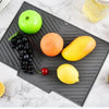 A silicone dish drying mat is placed on a marble surface, holding various fruits and vegetables like apples, lemons, tomatoes