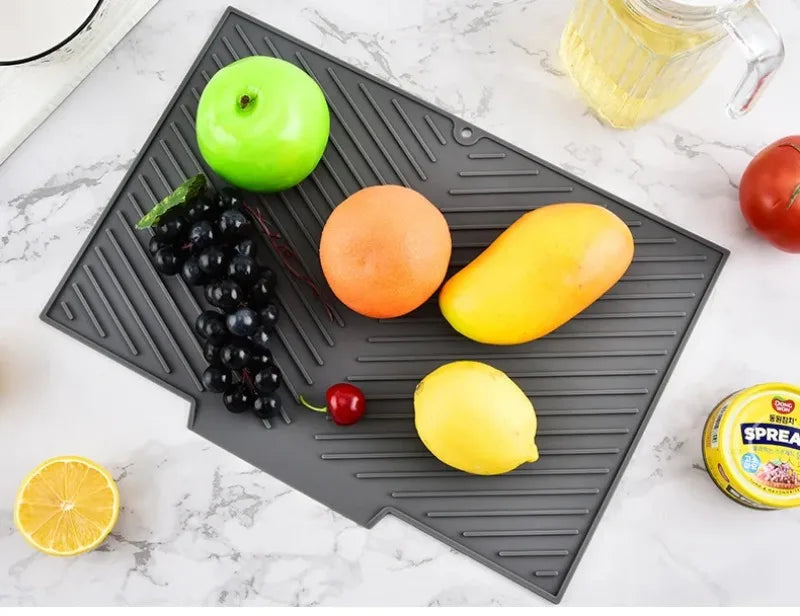 A silicone dish drying mat is placed on a marble surface, holding various fruits and vegetables like apples, lemons, tomatoes