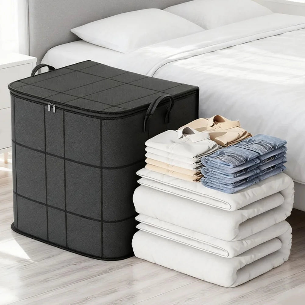 A black foldable wardrobe storage bag with a double zipper is placed next to a white bed with folded white linens.