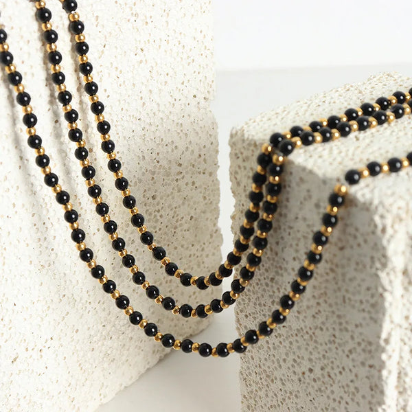 Rapprochement d'un collier de perles d'agate vintage avec des perles noires et dorées drapé sur une surface blanche texturée.