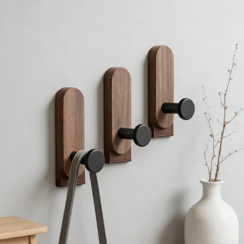 A set of three dark brown walnut wood adhesive hooks mounted on a white wall.