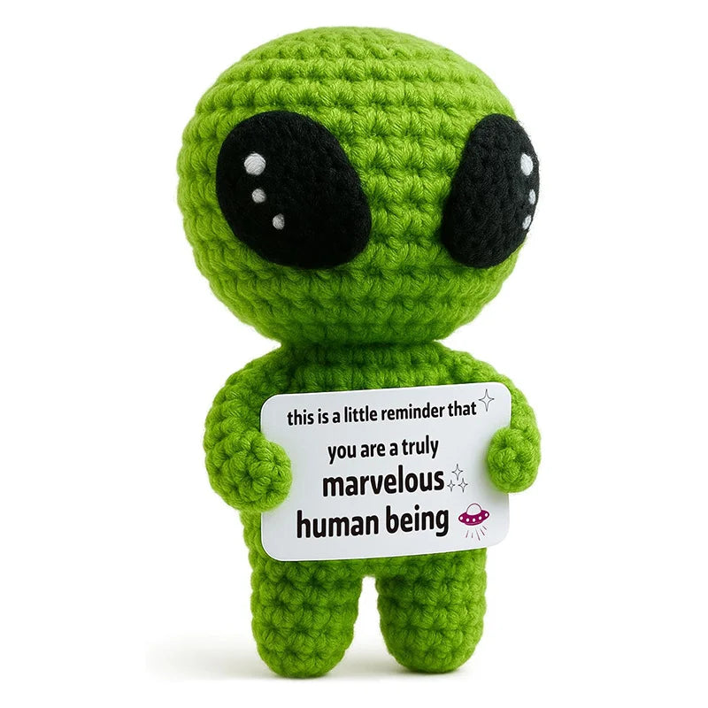A handmade crochet green alien doll with large black eyes holding a card that reads you are a truly marvelous human being