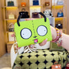 A hand holds a lime green cartoon print compact wallet with a black strap and gold keychain against a light wooden background