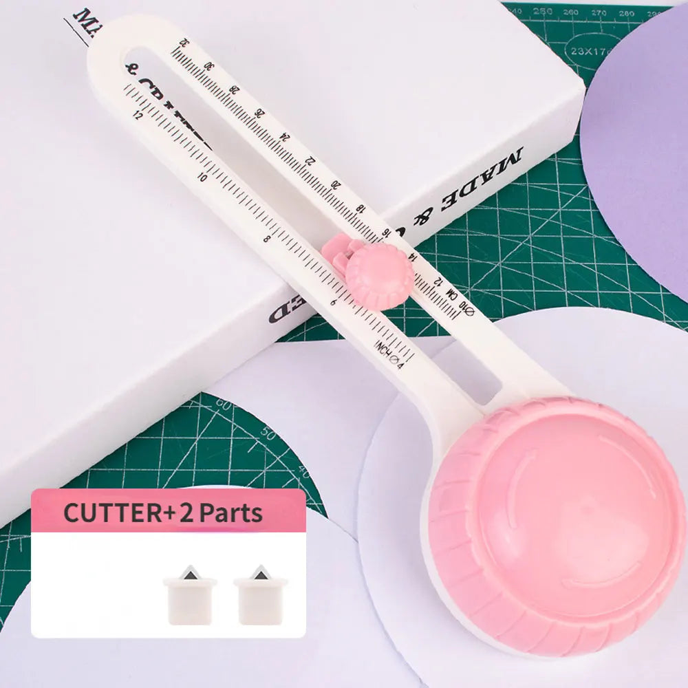 A white adjustable circular paper cutter tool with a pink blade and measuring markings is shown on a green surface.