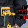 A yellow tape measure holder is clipped onto a black belt, demonstrating its use for measuring tape.