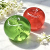A green fruit-shaped squeeze toy and a red fruit-shaped item are shown on a white marble surface.
