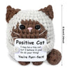A handmade crochet cat doll with brown and white fur, featuring a positive message card.