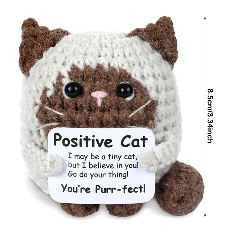 A handmade crochet cat doll with brown and white fur, featuring a positive message card.