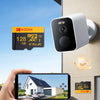 A white security camera is mounted on a wall, with a hand holding a smartphone displaying a live video feed from the camera.