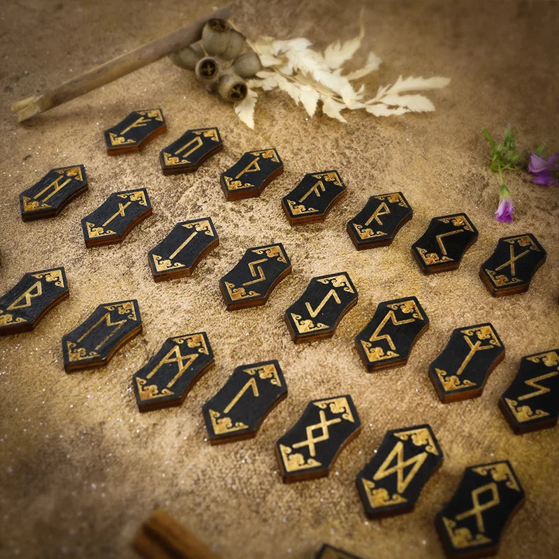 A collection of wooden rune stones arranged on sand with a wooden stick and dried leaves in the background.