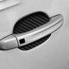 A close-up view of a silver car door handle with a black carbon fiber protective cover installed on the door.