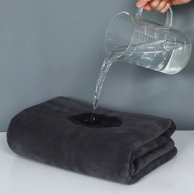 A clear glass pours water onto a dark gray microfiber bath towel.