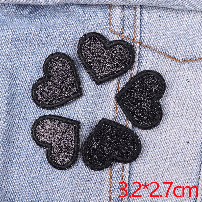 A set of five black and silver glitter heart iron-on embroidered patches on a denim fabric.