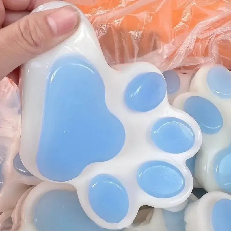 A white silicone cat paw squeeze toy with blue accents is shown in a hand, used as a fidget or stress relief item.